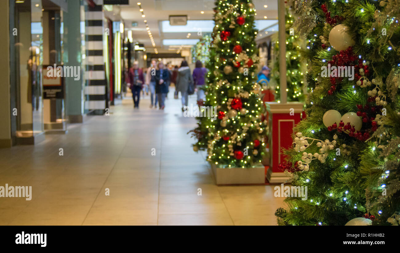 Shoppers in mall in distance with Christmas trees in focus in foreground. Stock Photo