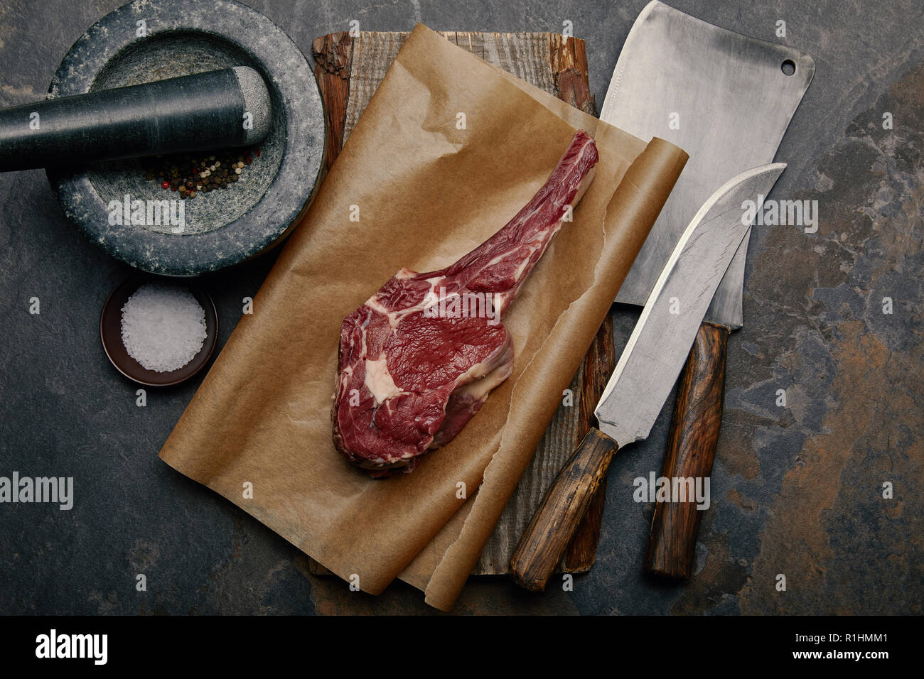 top view of raw rib eye steak on baking paper with kitchen knives and