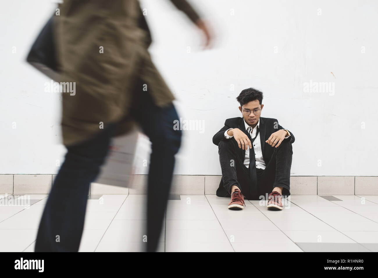 dowdy young asian businessman sitting at walkway thinking of his problem and look so depressed while people passing by ( motion blur ) Stock Photo