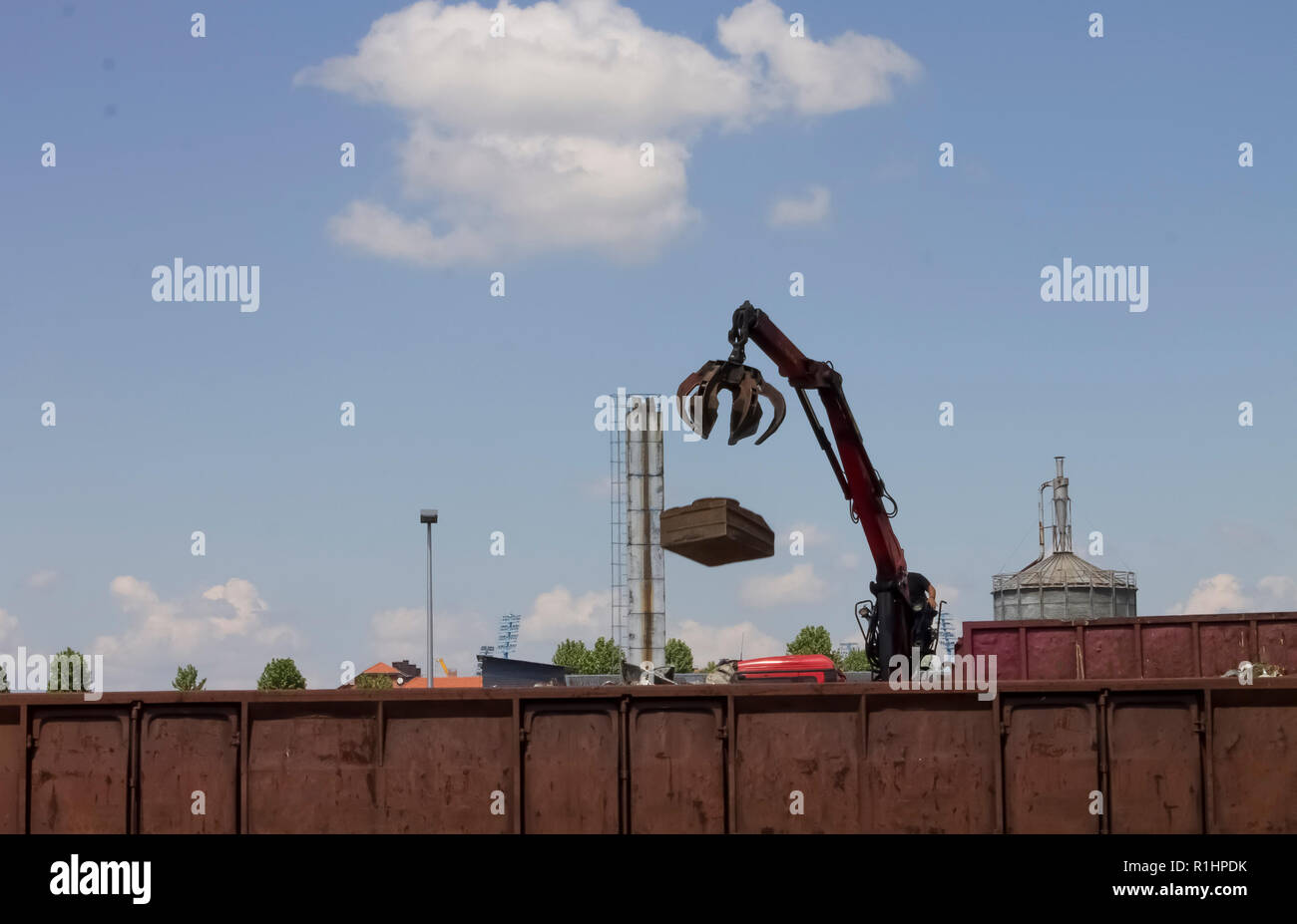 Red crane throwing metal industrial waste into a train container at ...