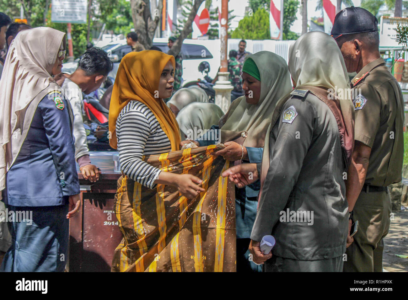 Islamic Sharia Police Officer (Wilayatul Hisbah) is seen tying a sarong to a woman who violated the Islamic Sharia law by force in the city of Lhokseumawe. Islamic Sharia Police Officers (Wilayatul Hisbah) provide sarongs for those who violated the Islamic Sharia law by force in the city of Lhokseumawe, Aceh is the only province in Indonesia that has the largest population of Muslims in the world, which implements the Islamic Sharia law such as committee caning and conducting routine raids for those who are tightly dressed for women and shorts for men. Stock Photo