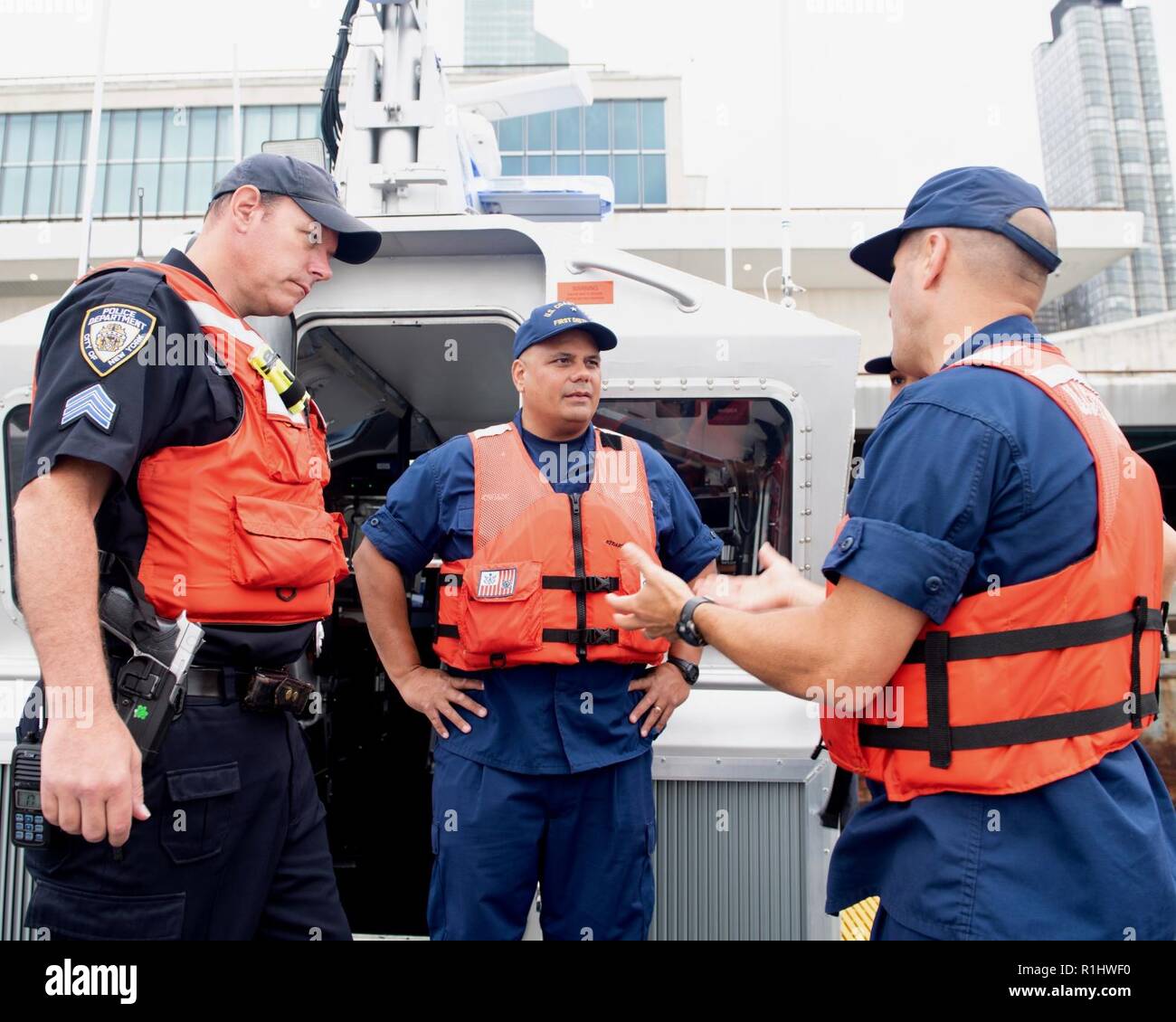 NEW YORK – Rear Adm. Andrew J. Tiongson, commander, First Coast Guard District (center) and Capt. Jason P. Tama, commander Coast Guard Sector New York (right), converse with a member of the New York City Police Department Harbor Unit on the East River during a mass casualty drill conducted outside the United Nations Building, Sept. 21, 2018. The Coast Guard along with multiple agencies, support maritime safety and security during the country’s largest National Special Security Event (NSSE). Stock Photo