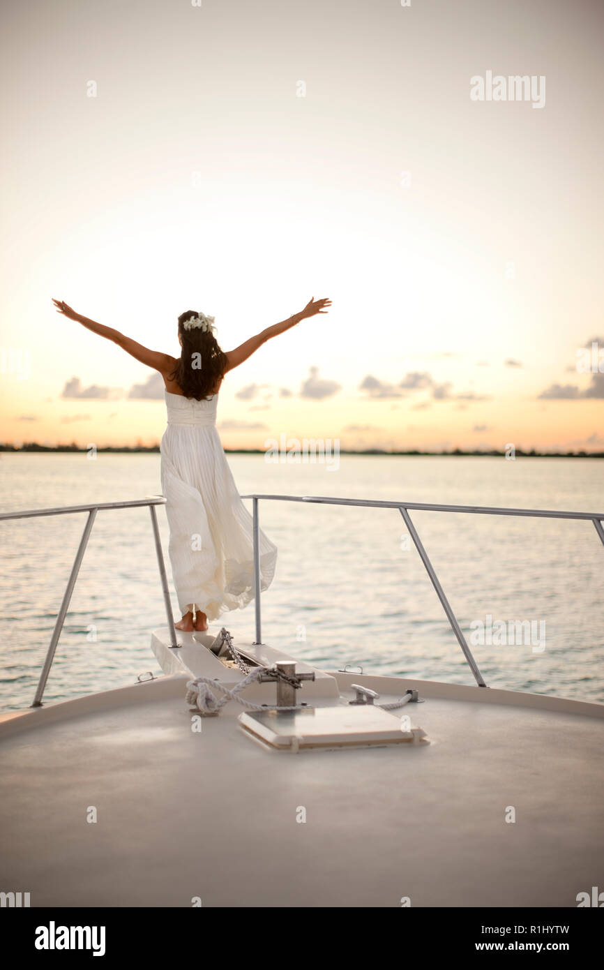 Bride standing on the prow of a boat with her arms in the air. Stock Photo