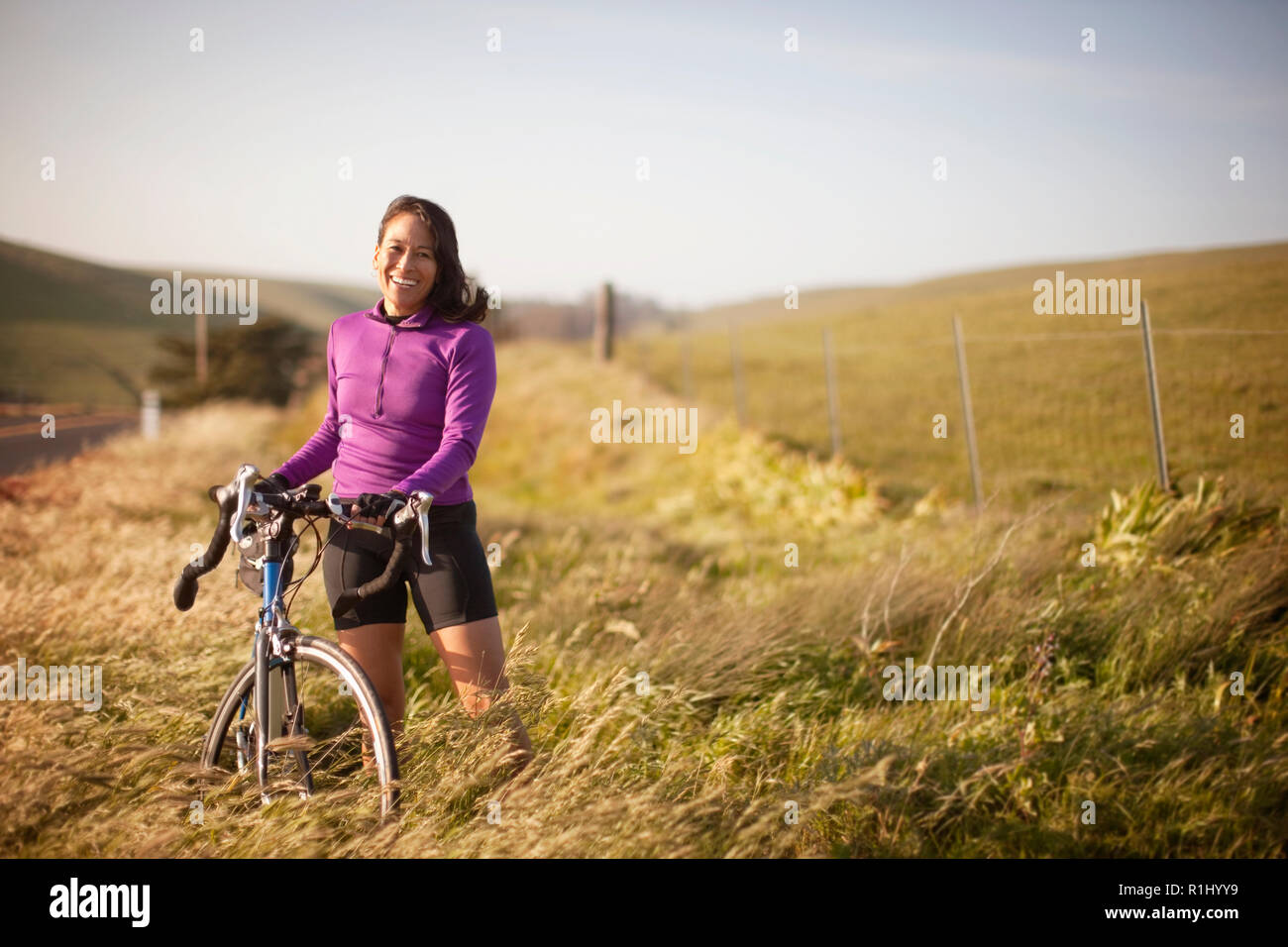 Middle aged women stands with her bicycle next to a wire fence in the countryside. Stock Photo