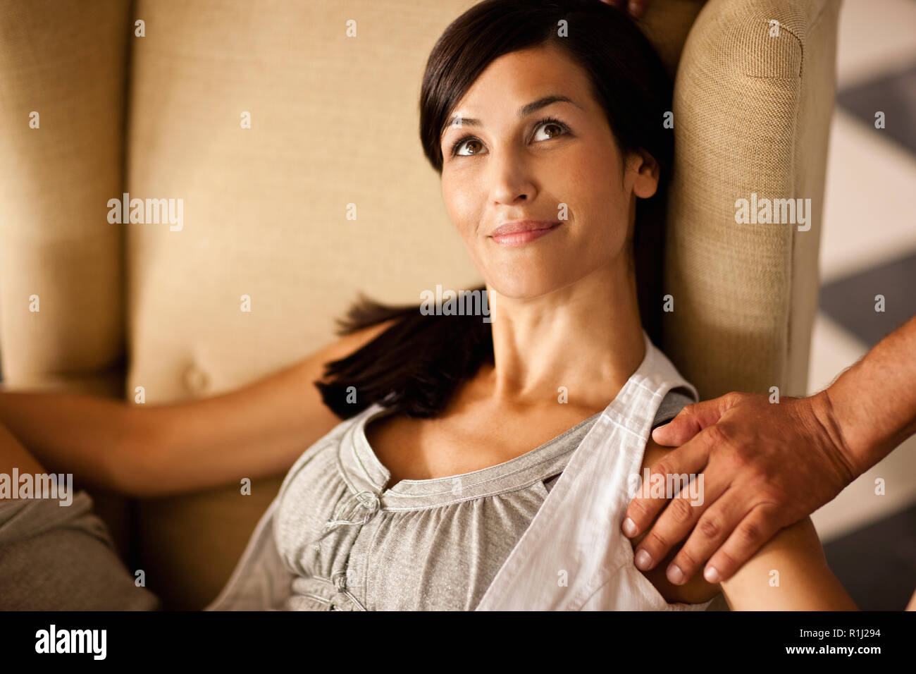 Mid-adult woman relaxing on armchair with a male hand on her shoulder. Stock Photo