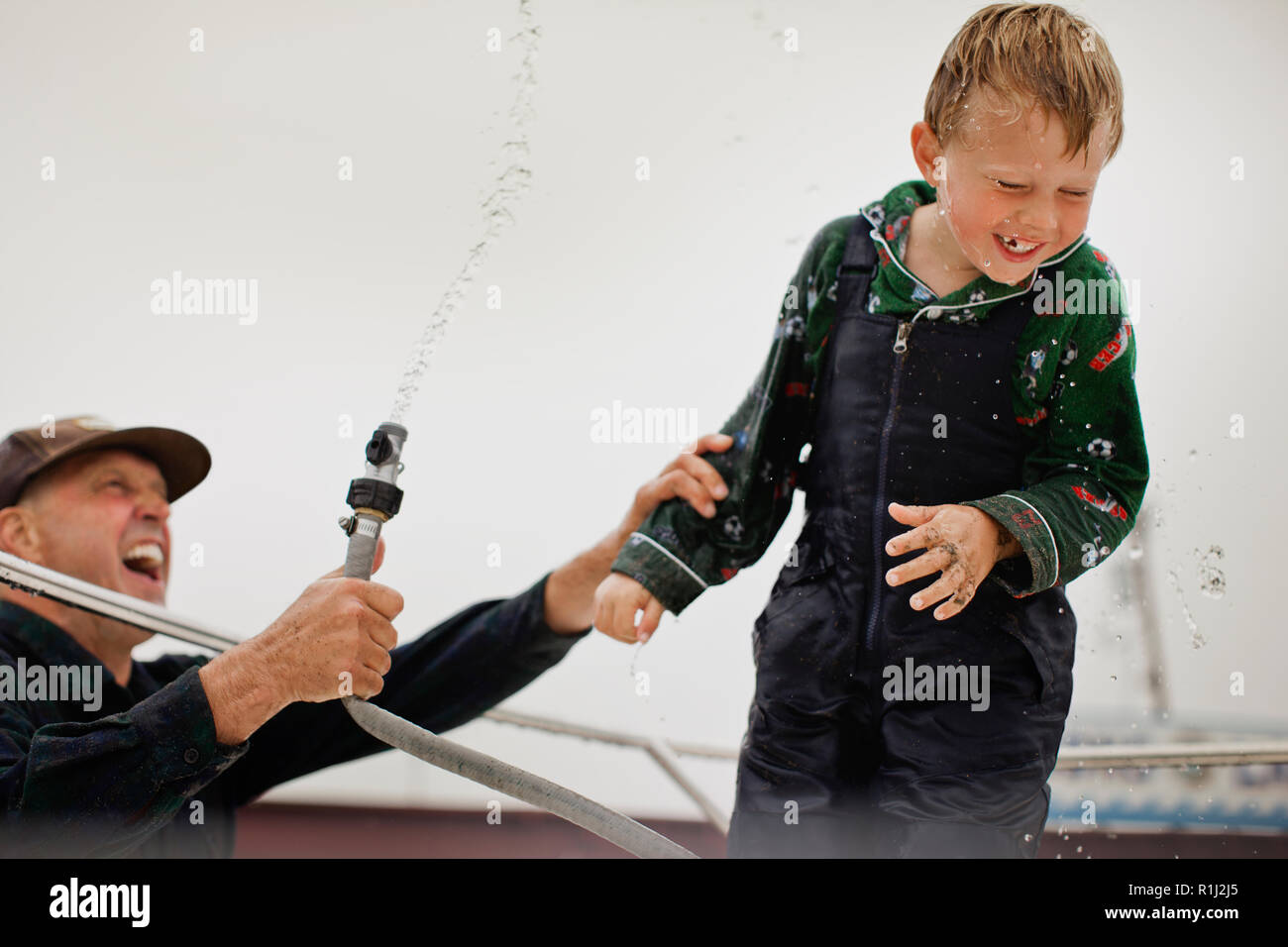 Mature man squirts his young son with garden hose. Stock Photo