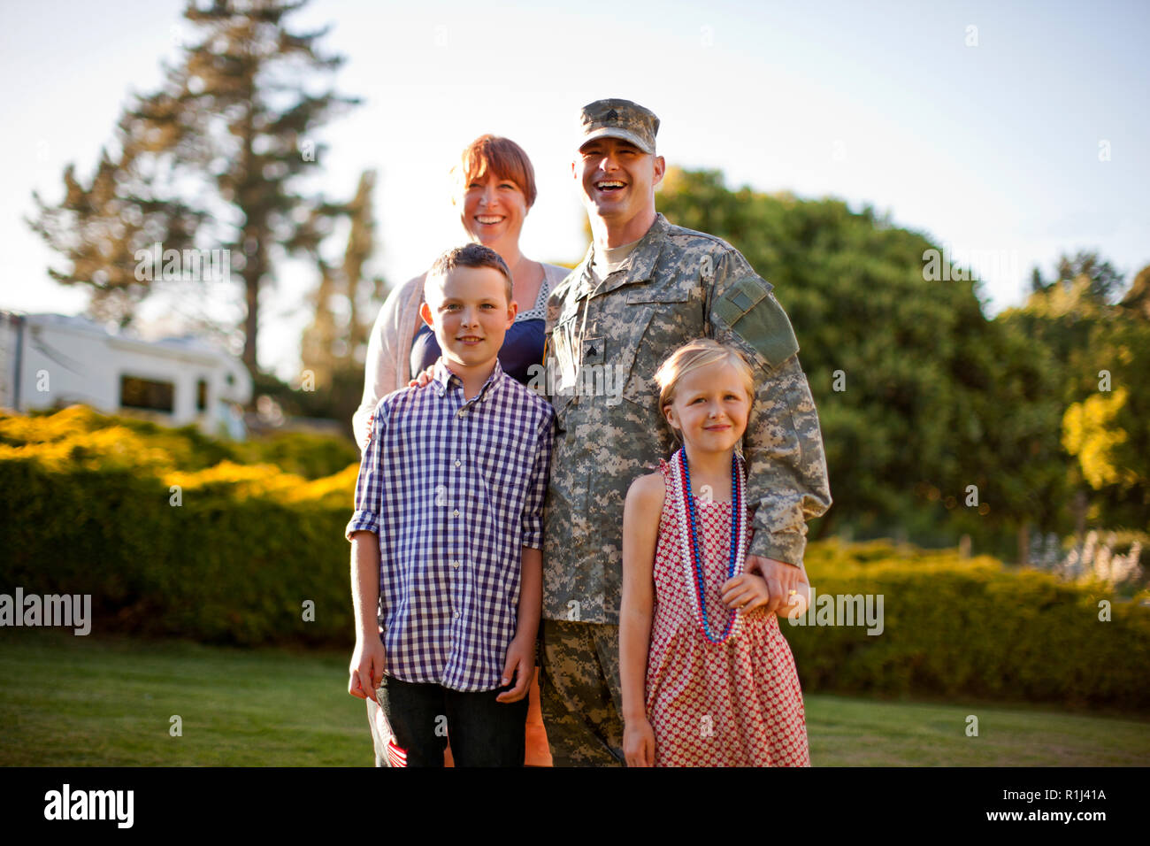 Portrait of a smiling male soldier standing with his family in the back yard of their home. Stock Photo