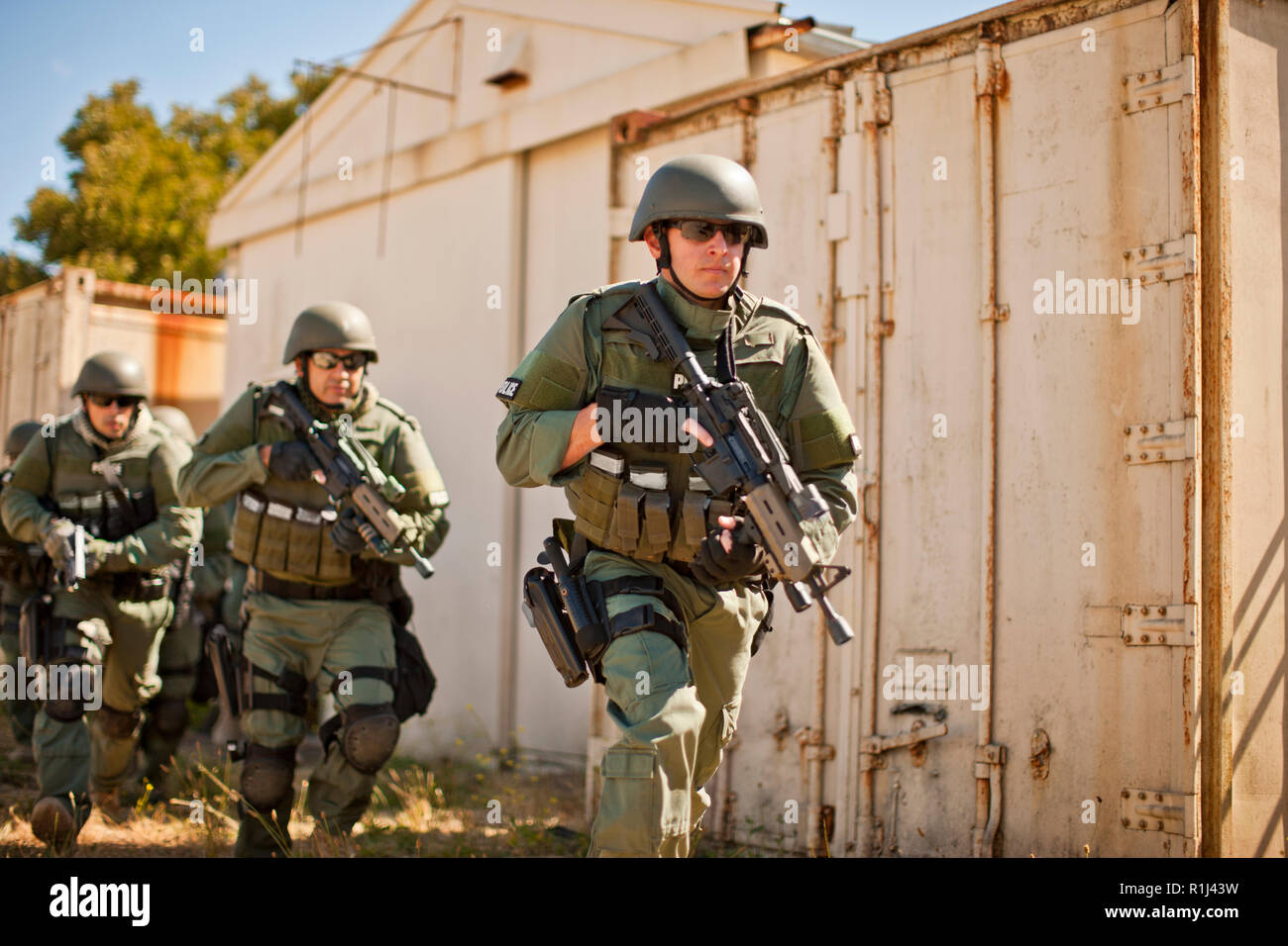 Team of armed military police holding guns while running through a battle zone. Stock Photo