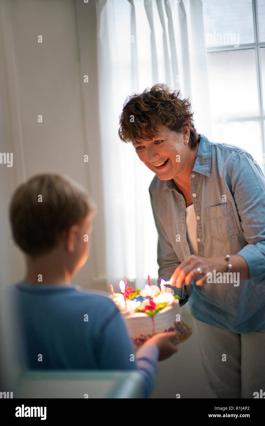 Smiling mature woman lighting the candles on a birthday cake. Stock Photo