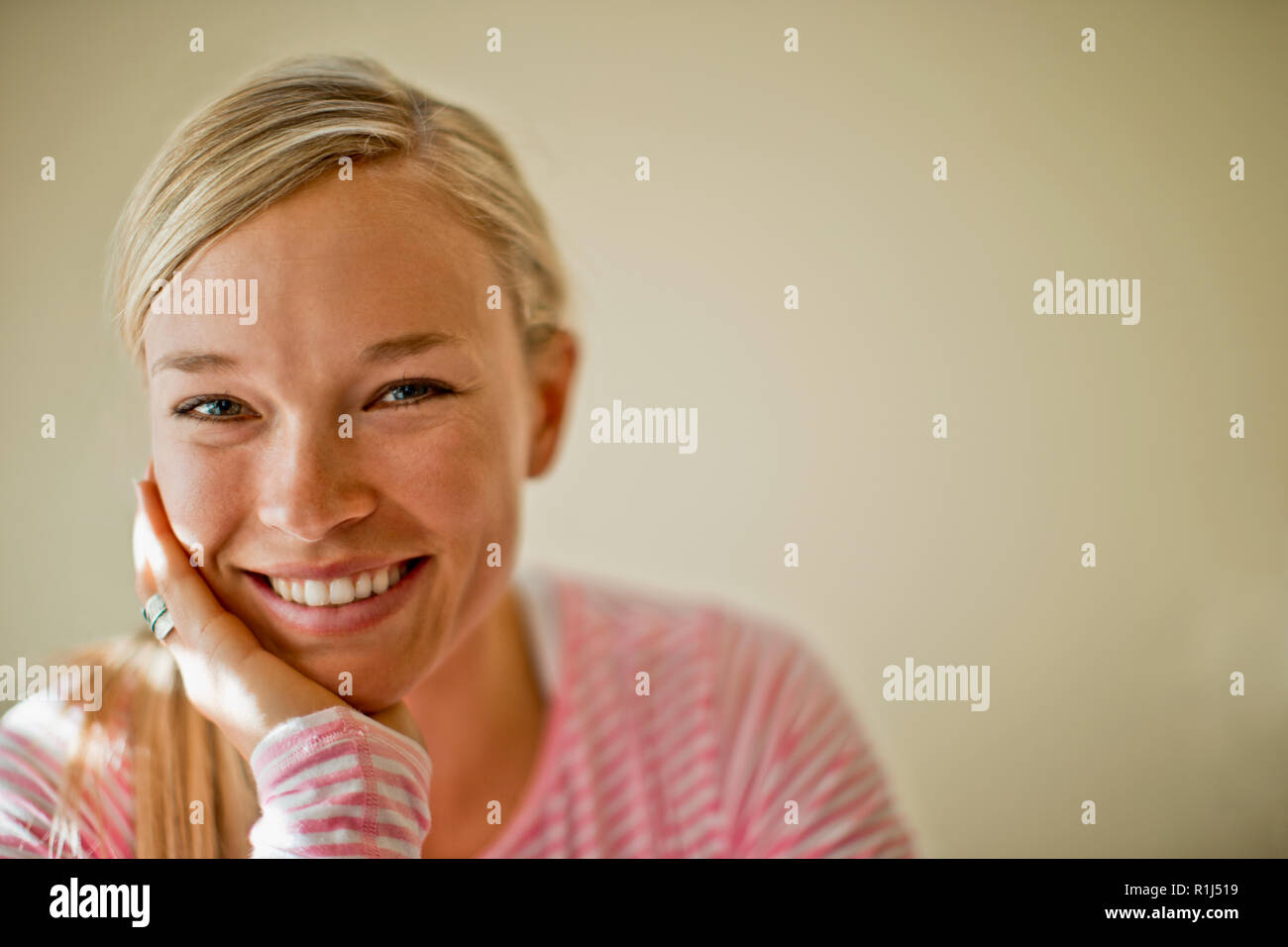 Cheerful young woman smiles as she rests her chin on her hand. Stock Photo