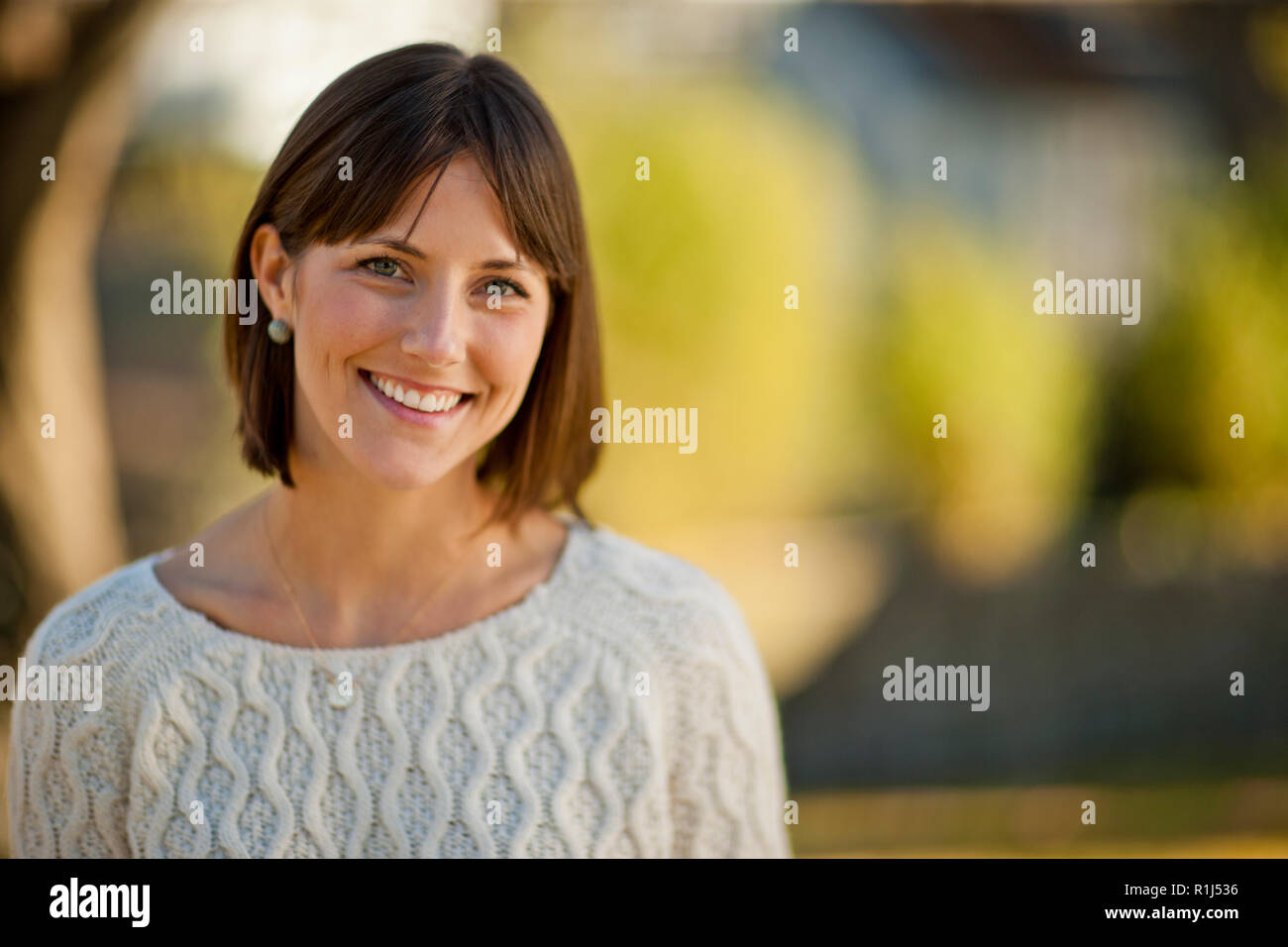 Portrait of a smiling young woman relaxing in a sunlit garden. Stock Photo