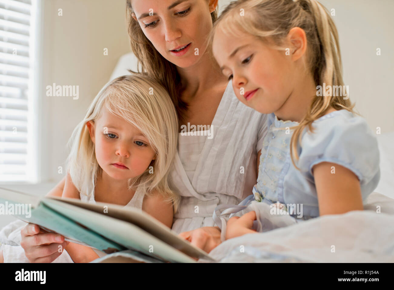 Mother sitting on a bed reading a book with her daughters. Stock Photo
