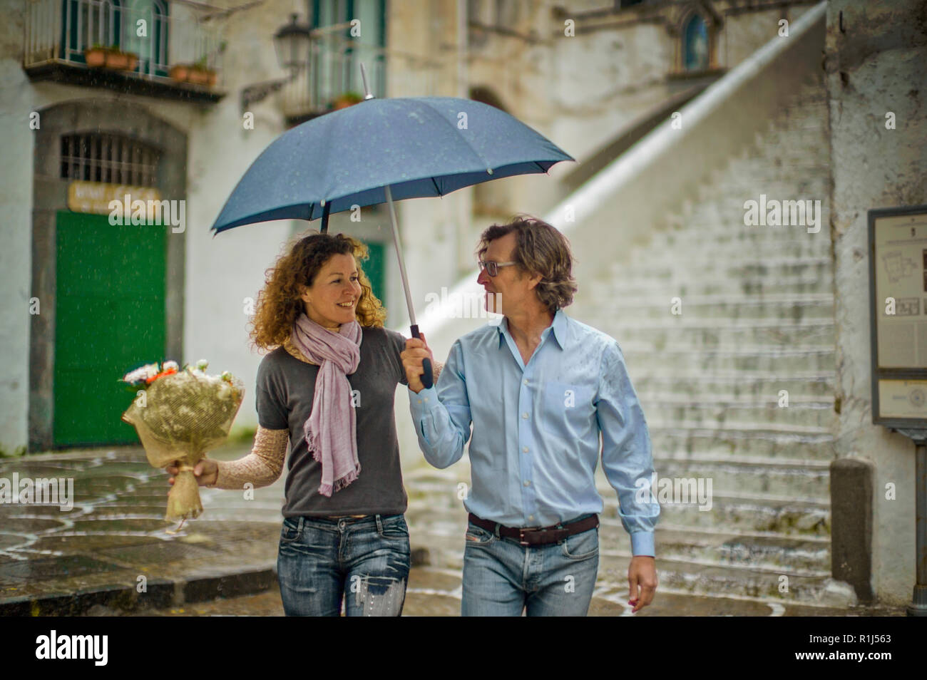 Smiling middle aged couple sheltering under an umbrella. Stock Photo