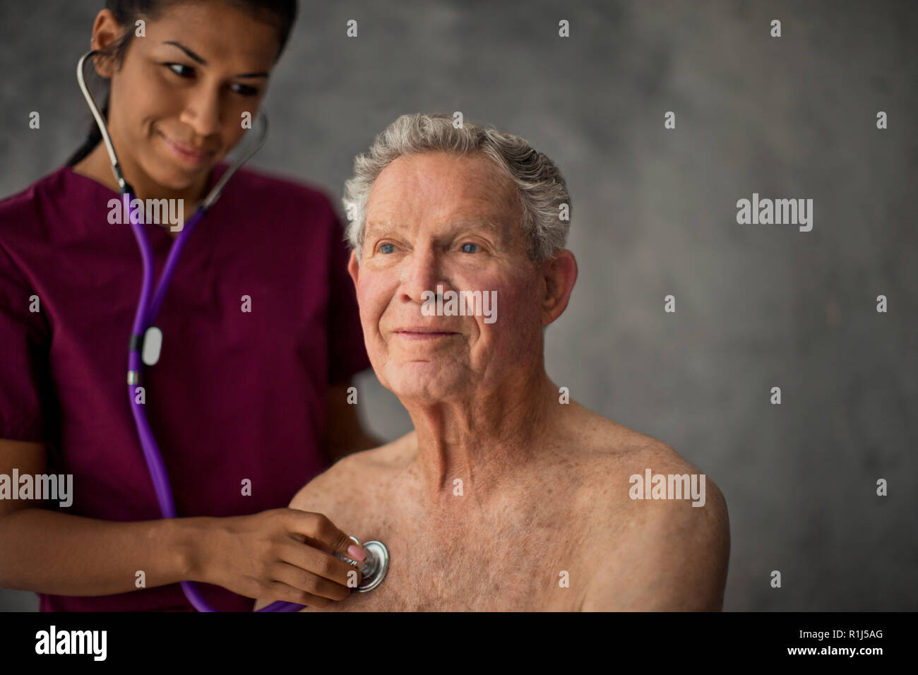 Happy young nurse listening to a senior patient's heartbeat. Stock Photo