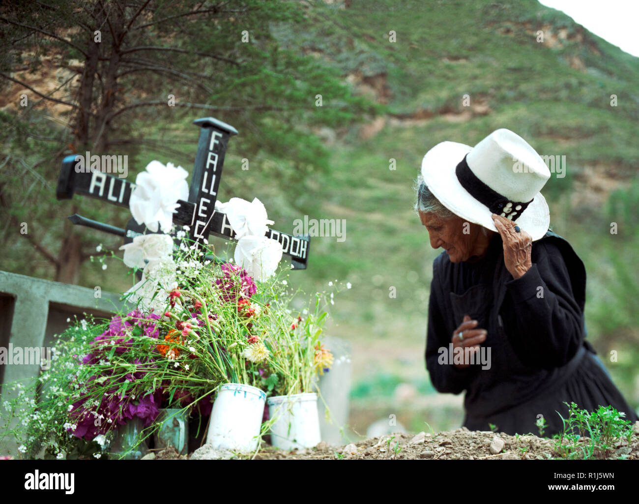 Grieving old woman taking off hat at a loved ones grave Stock Photo