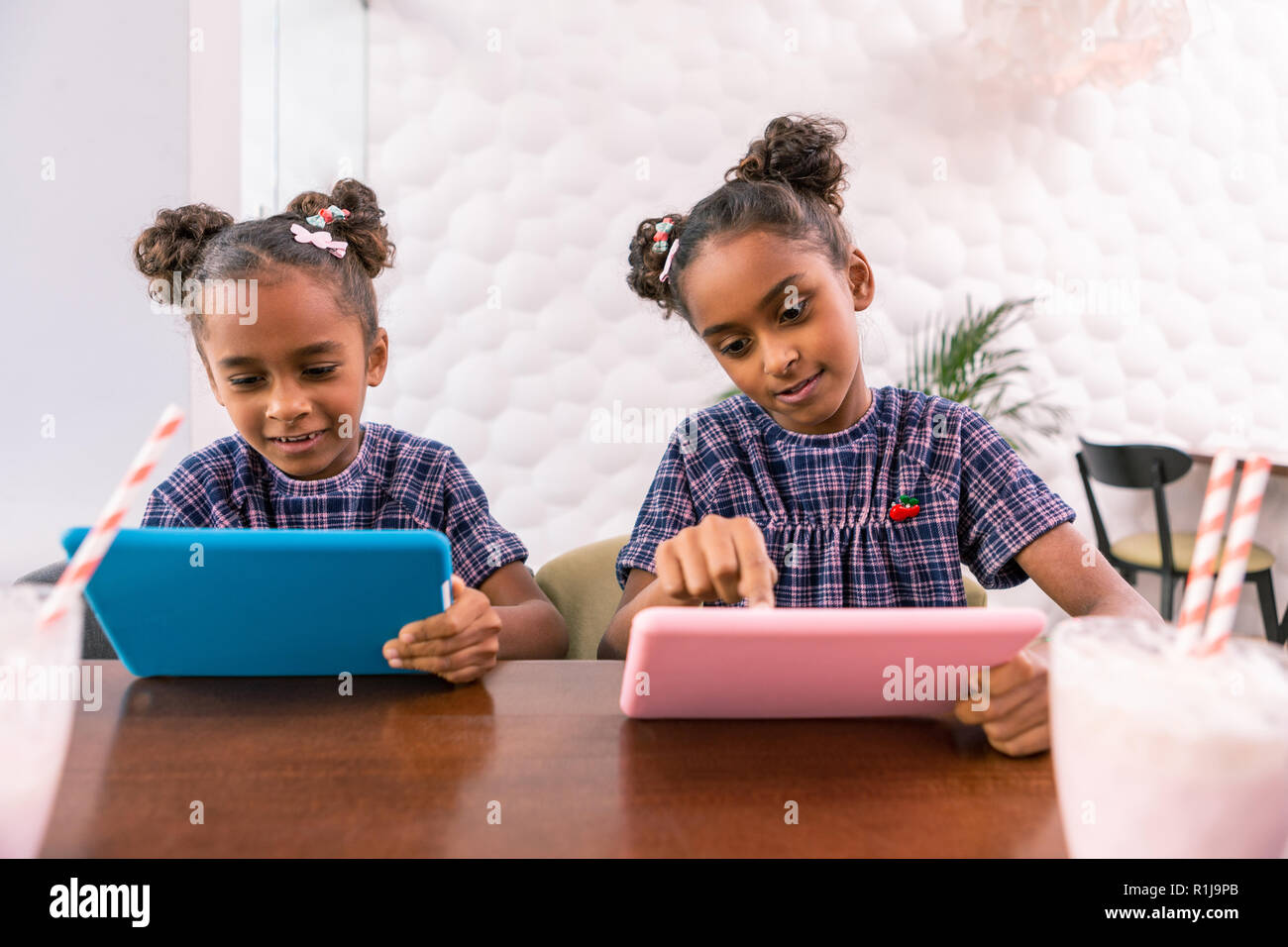 Cute siblings having the same hairstyles holding pink and blue tablets Stock Photo