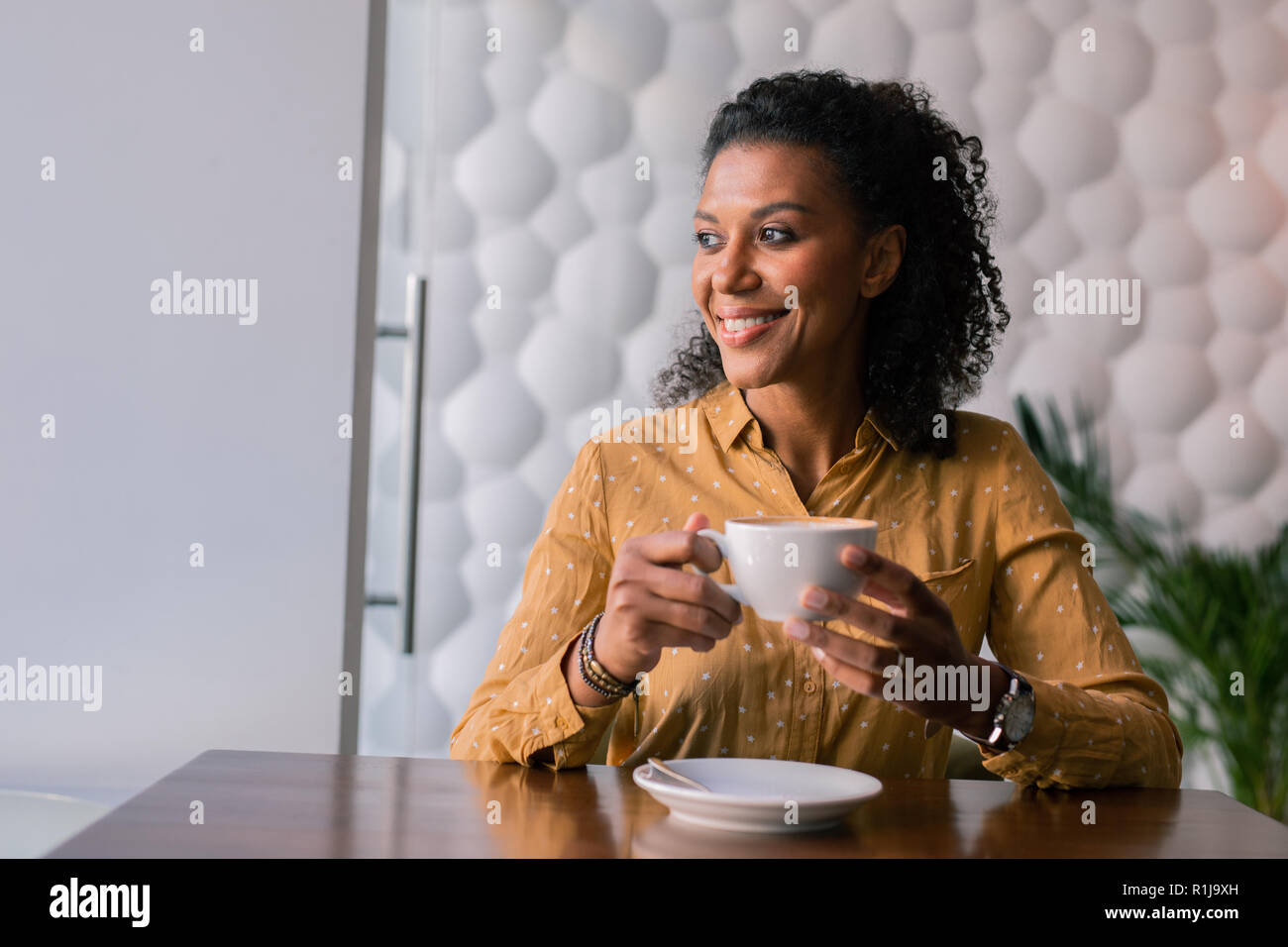 Beaming dark-eyed woman looking at window while drinking some coffee Stock Photo