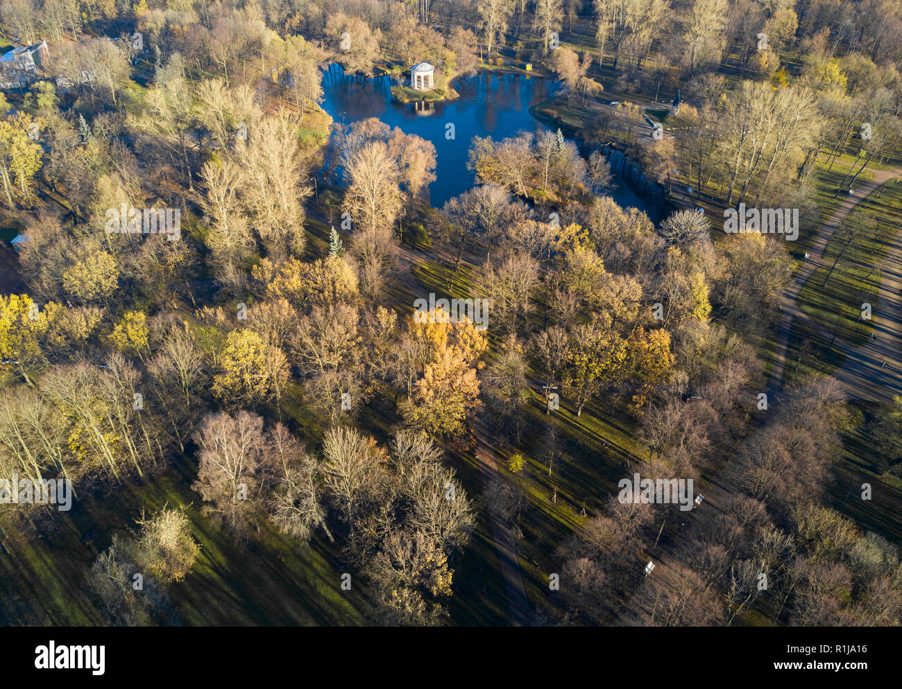 Aerial; drone view of autumn morning in beautiful city park; rest and recreation area with blue water lake and tall trees with long shadows; pretty st Stock Photo