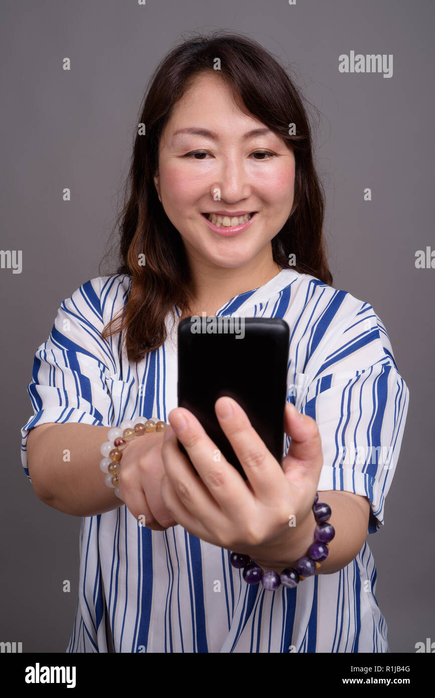 Mature beautiful Asian businesswoman using mobile phone Stock Photo