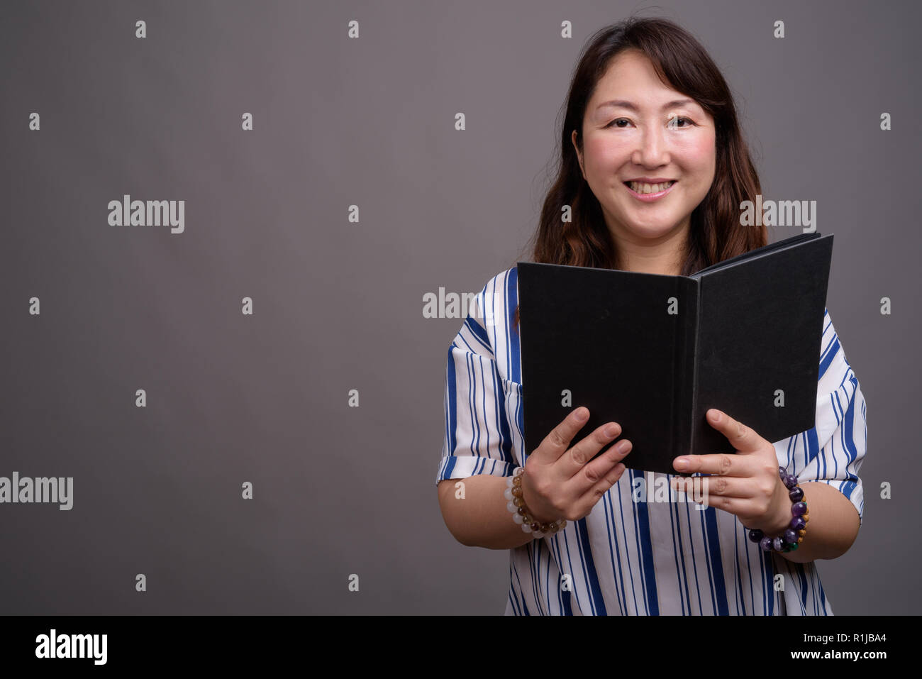 Portrait of mature beautiful Asian businesswoman reading book Stock Photo