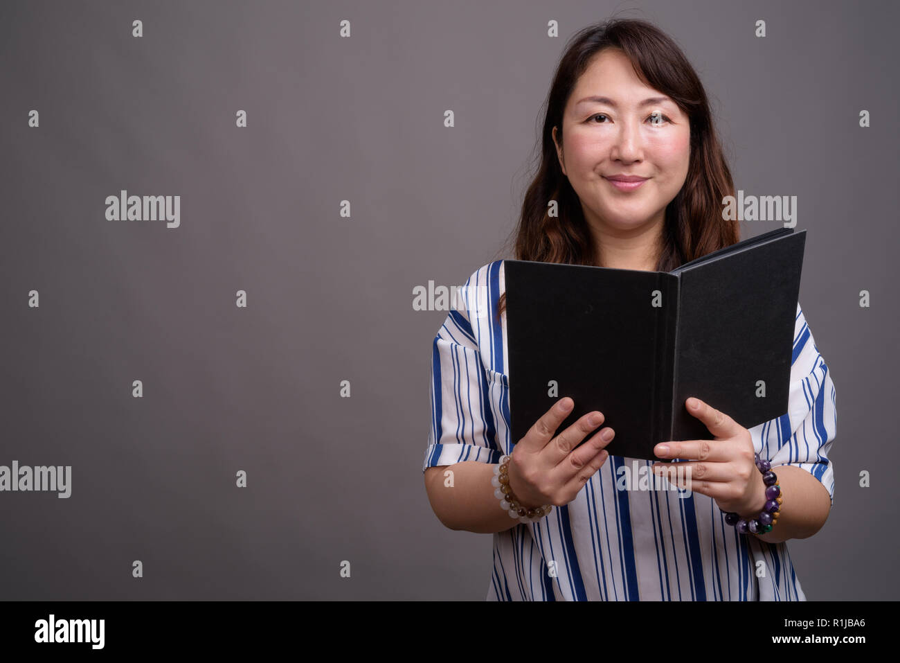 Portrait of mature beautiful Asian businesswoman reading book Stock Photo