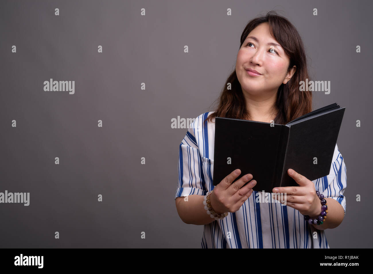 Portrait of mature beautiful Asian businesswoman reading book Stock Photo