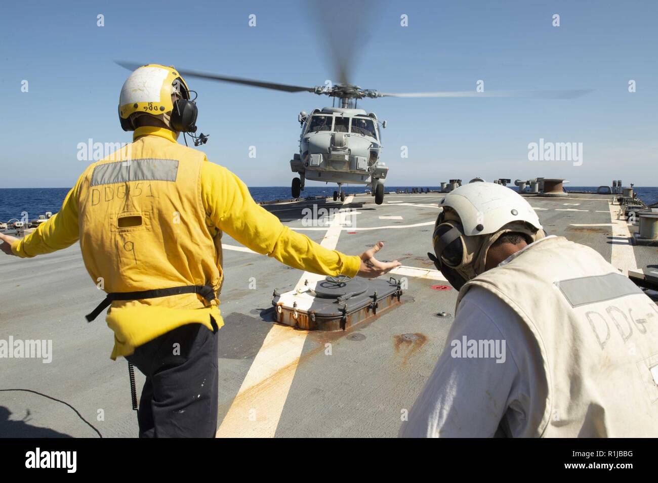 MEDITERRANEAN SEA (Oct. 4, 2018) Boatswain’s Mate 3rd Class Alexander Stiffler, left, directs a MH-60R Sea Hawk, assigned to the “Vipers” of Helicopter Maritime Strike Squadron (HSM) 48 aboard the Arleigh Burke-class guided-missile destroyer USS Arleigh Burke (DDG 51) in the Mediterranean Sea Oct. 4, 2018. Arleigh Burke, homeported at Naval Station Norfolk, is conducting naval operations in the U.S. 6th Fleet area of operations in support of U.S. national security interests in Europe and Africa. Stock Photo