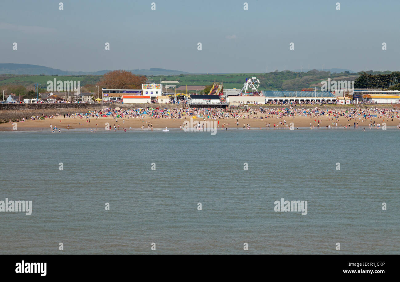 Crowded Bank Holiday beach at Sandy Bay, with Coney Beach Pleasure Park behiind, Porthcawl, Bridgend, South Wales, UK Stock Photo