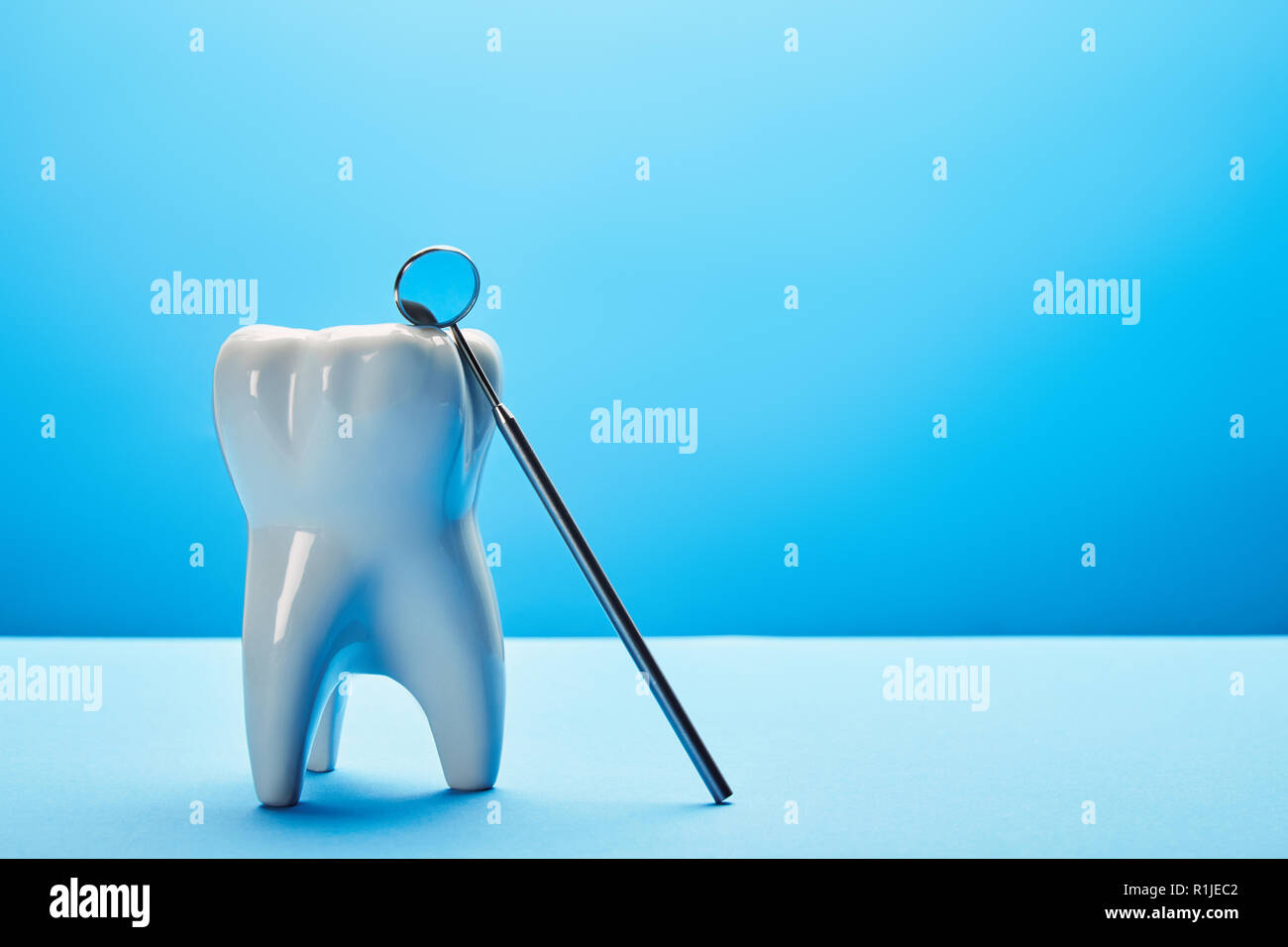 close up view of tooth model and dental mouth mirror on blue backdrop ...