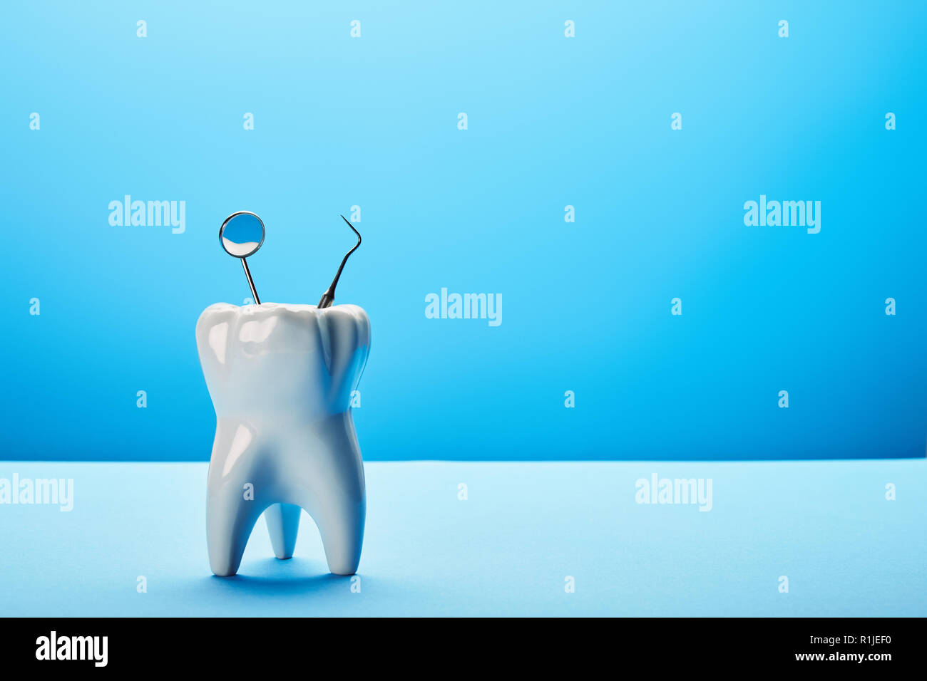 close up view of tooth model, dental mirror and probe on blue backdrop ...