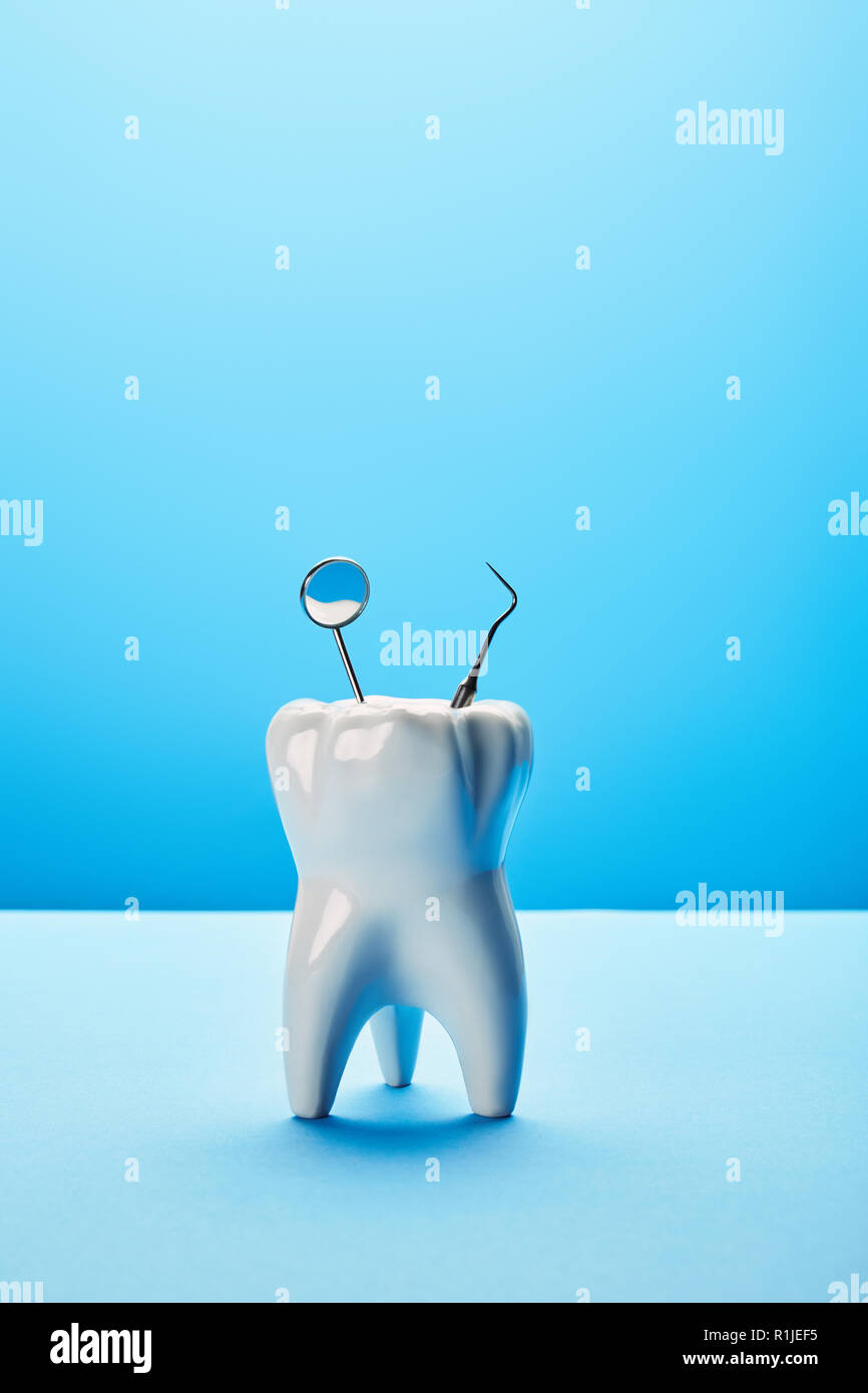 close up view of tooth model, dental mirror and probe on blue backdrop ...