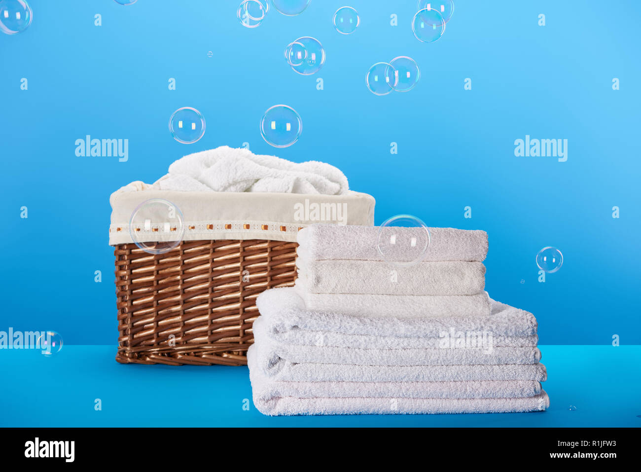 Laundry basket filled white fluffy towels, cotton flowers and a bottle of  liquid soap against a blurred grey background Stock Photo - Alamy