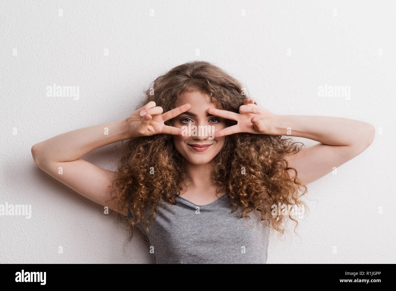 Young beautiful cheerful woman in studio, fingers forming V. Stock Photo