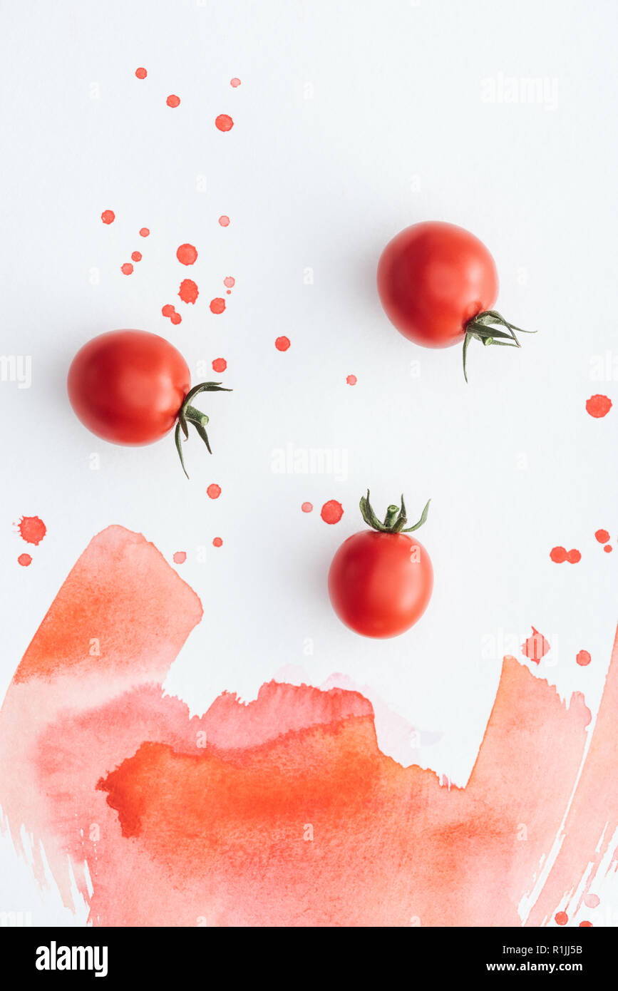 top view of ripe cherry tomatoes on white surface with red watercolor strokes and blots Stock Photo