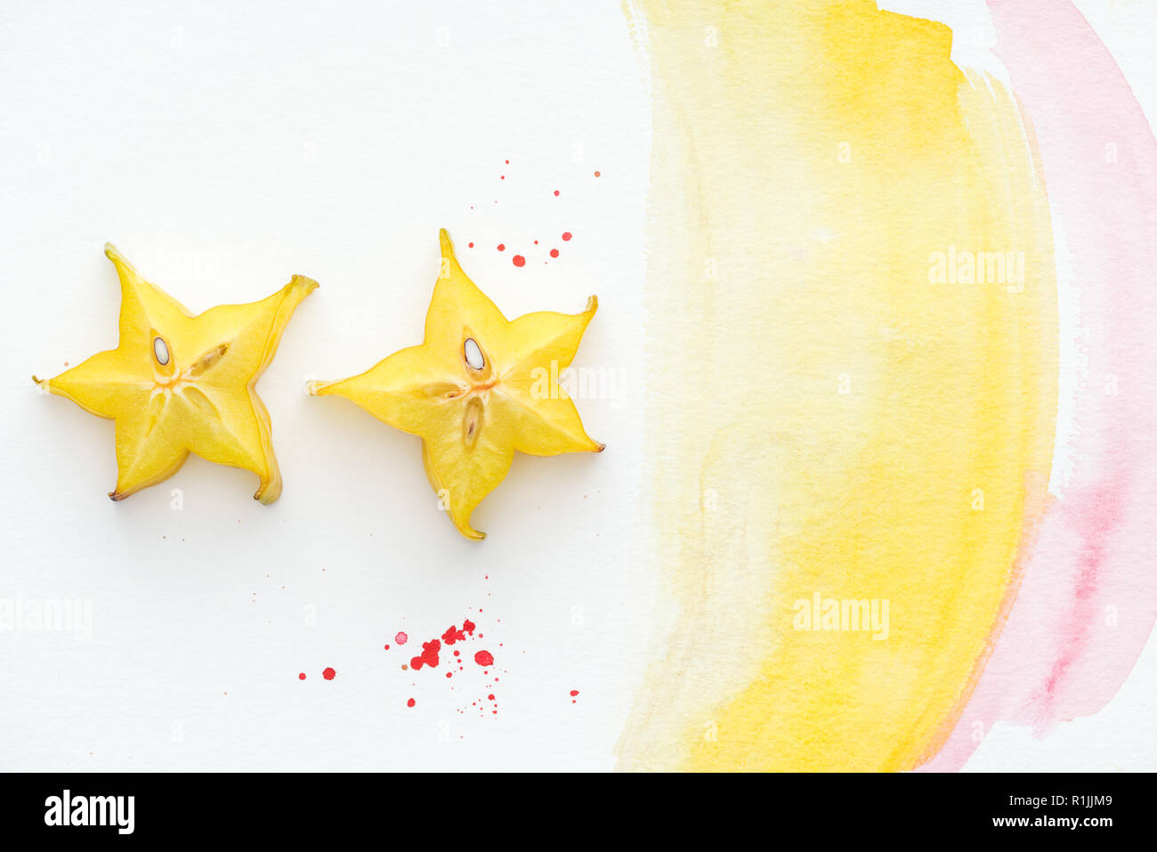 top view of two exotic star fruits on white surface with yellow and pink watercolor Stock Photo
