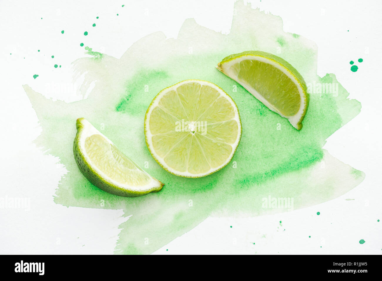 top view of pieces of green ripe limes on white surface with green watercolor Stock Photo