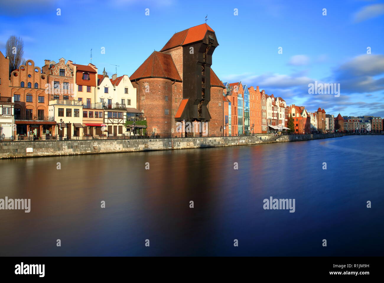 Panorama of Gdansk historical downtown, river, shore with beautiful architecture, medieval crane, skyline, blue sky with few clouds, long exposure. Stock Photo