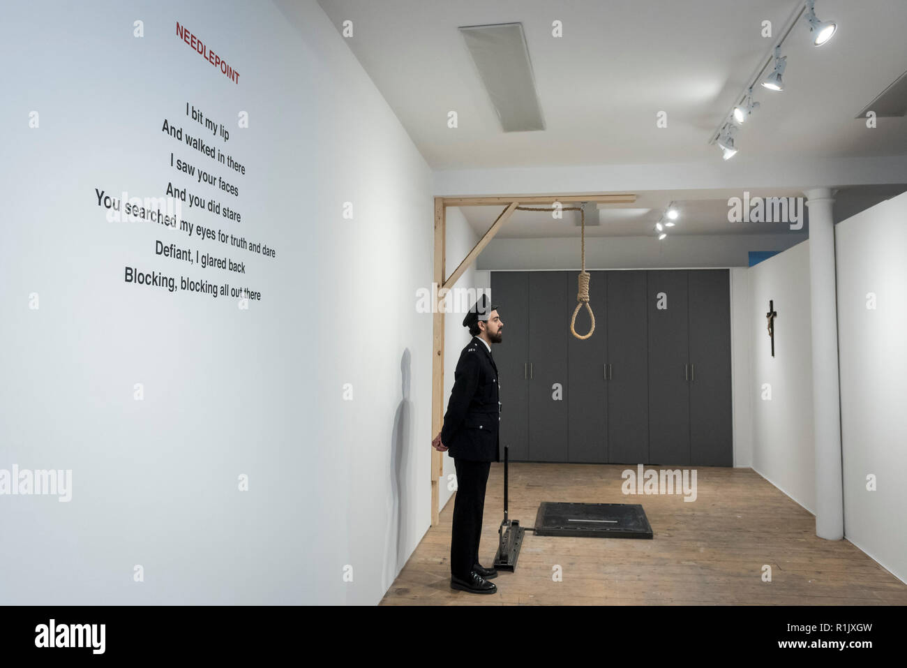 London, UK.  13 November 2018. The artist's poerty on a wall next to a staff member, posing as a prison guard, and the hangman's noose.  Preview of 'Glad I Did It', a new work by Irish artist Christina Reihill at Bermondsey Project Space.  The interactive artwork looks at the life and death of Ruth Ellis, the last woman to be hanged in Britain, after she shot her lover, racing driver, David Blakely in 1955.  On display are the artist's interpretation of Ruth Ellis' prison cell, including furniture and props, the hanging room together with a video display of the artist in conversation. Credit:  Stock Photo