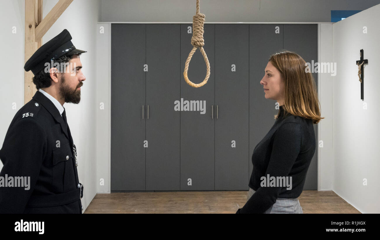 London, UK.  13 November 2018. Staff members, one posing as a prison guard, view a hangman's noose.  Preview of 'Glad I Did It', a new work by Irish artist Christina Reihill at Bermondsey Project Space.  The interactive artwork looks at the life and death of Ruth Ellis, the last woman to be hanged in Britain, after she shot her lover, racing driver, David Blakely in 1955.  On display are the artist's interpretation of Ruth Ellis' prison cell, including furniture and props, the hanging room together with a video display of the artist in conversation. Credit: Stephen Chung/Alamy Live News Stock Photo