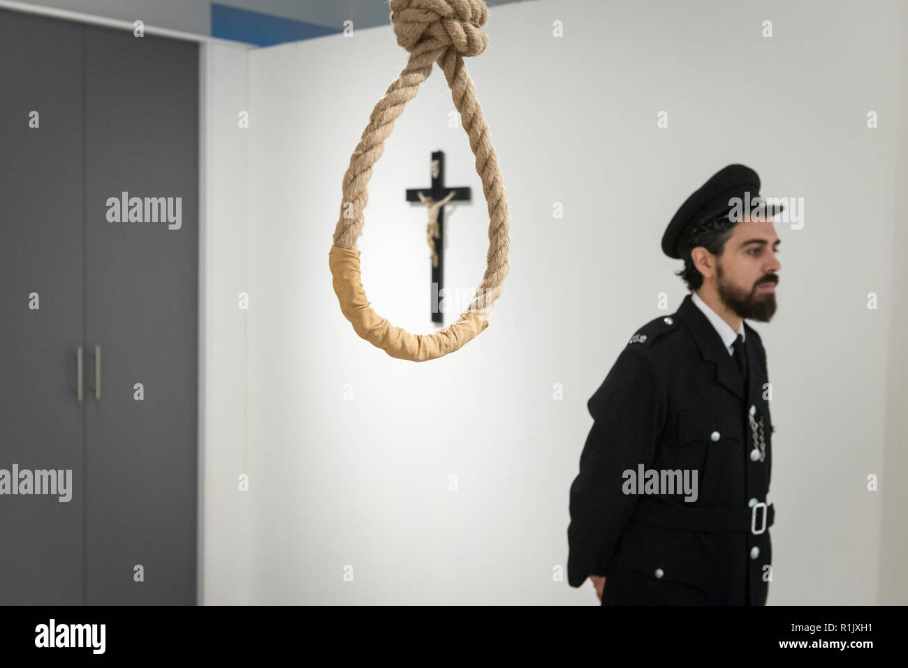 London, UK.  13 November 2018. A staff member, posing as a prison guard, views a hangman's noose.  Preview of 'Glad I Did It', a new work by Irish artist Christina Reihill at Bermondsey Project Space.  The interactive artwork looks at the life and death of Ruth Ellis, the last woman to be hanged in Britain, after she shot her lover, racing driver, David Blakely in 1955.  On display are the artist's interpretation of Ruth Ellis' prison cell, including furniture and props, the hanging room together with a video display of the artist in conversation. Credit: Stephen Chung/Alamy Live News Stock Photo