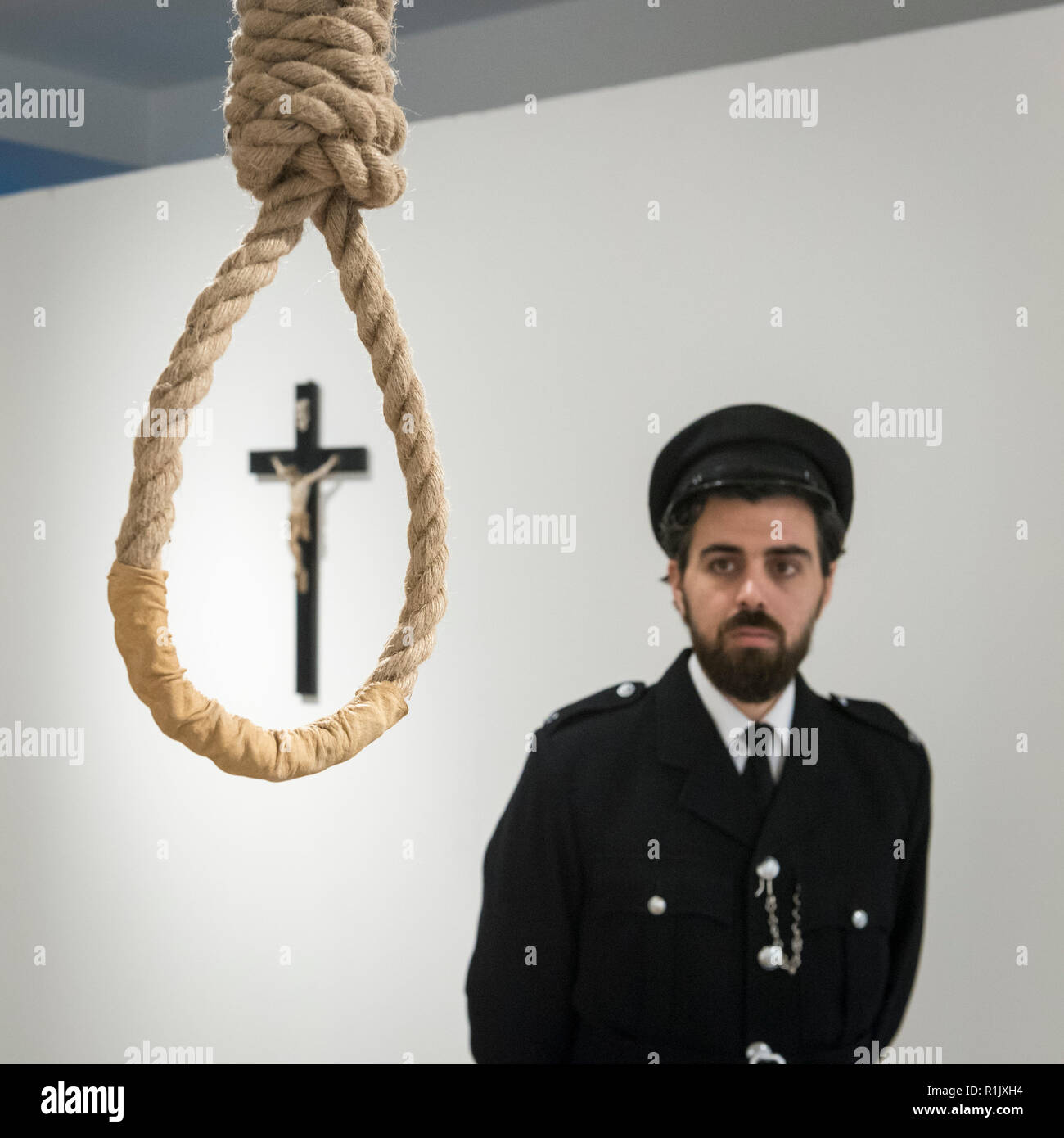 London, UK.  13 November 2018. A staff member, posing as a prison guard, views a hangman's noose.  Preview of 'Glad I Did It', a new work by Irish artist Christina Reihill at Bermondsey Project Space.  The interactive artwork looks at the life and death of Ruth Ellis, the last woman to be hanged in Britain, after she shot her lover, racing driver, David Blakely in 1955.  On display are the artist's interpretation of Ruth Ellis' prison cell, including furniture and props, the hanging room together with a video display of the artist in conversation. Credit: Stephen Chung/Alamy Live News Stock Photo