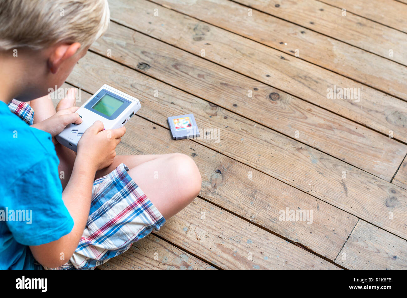 Young boy using his nintendo gameboy to play computer games. Nineties setting. indoors setting. Stock Photo