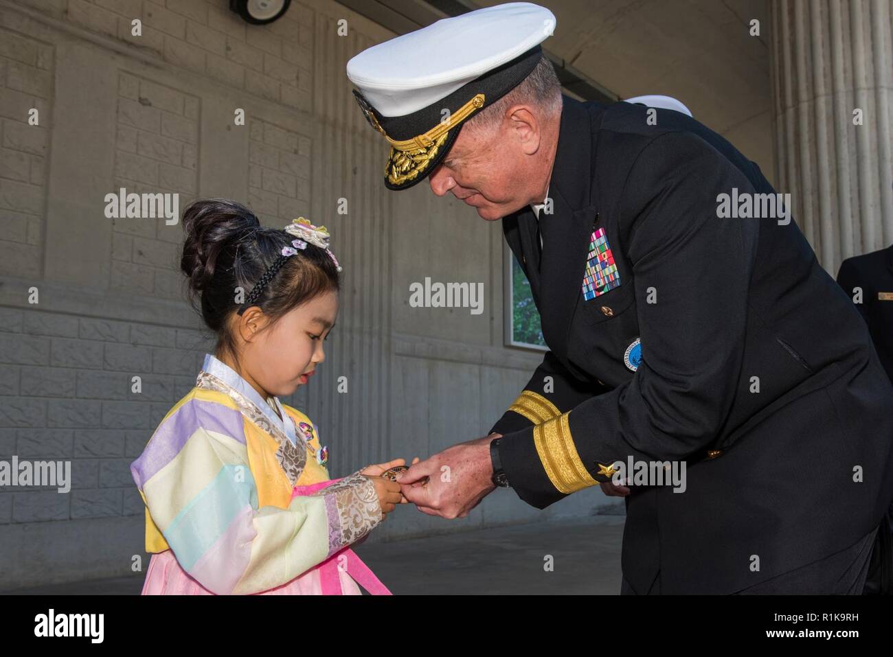 JEJU ISLAND, Republic of Korea, (Oct. 12, 2018) Rear Adm. Michael E. Boyle, commander, U.S. Naval Forces Korea (CNFK) presents a coin to a young girl during a welcome ceremony at the Republic of Korea (ROK) Navy base in Jeju. CNFK is the U.S. Navy's representative in the ROK, providing leadership and expertise in naval matters to improve institutional and operational effectiveness between the two navies and to strengthen collective security efforts in Korea and the region. Stock Photo