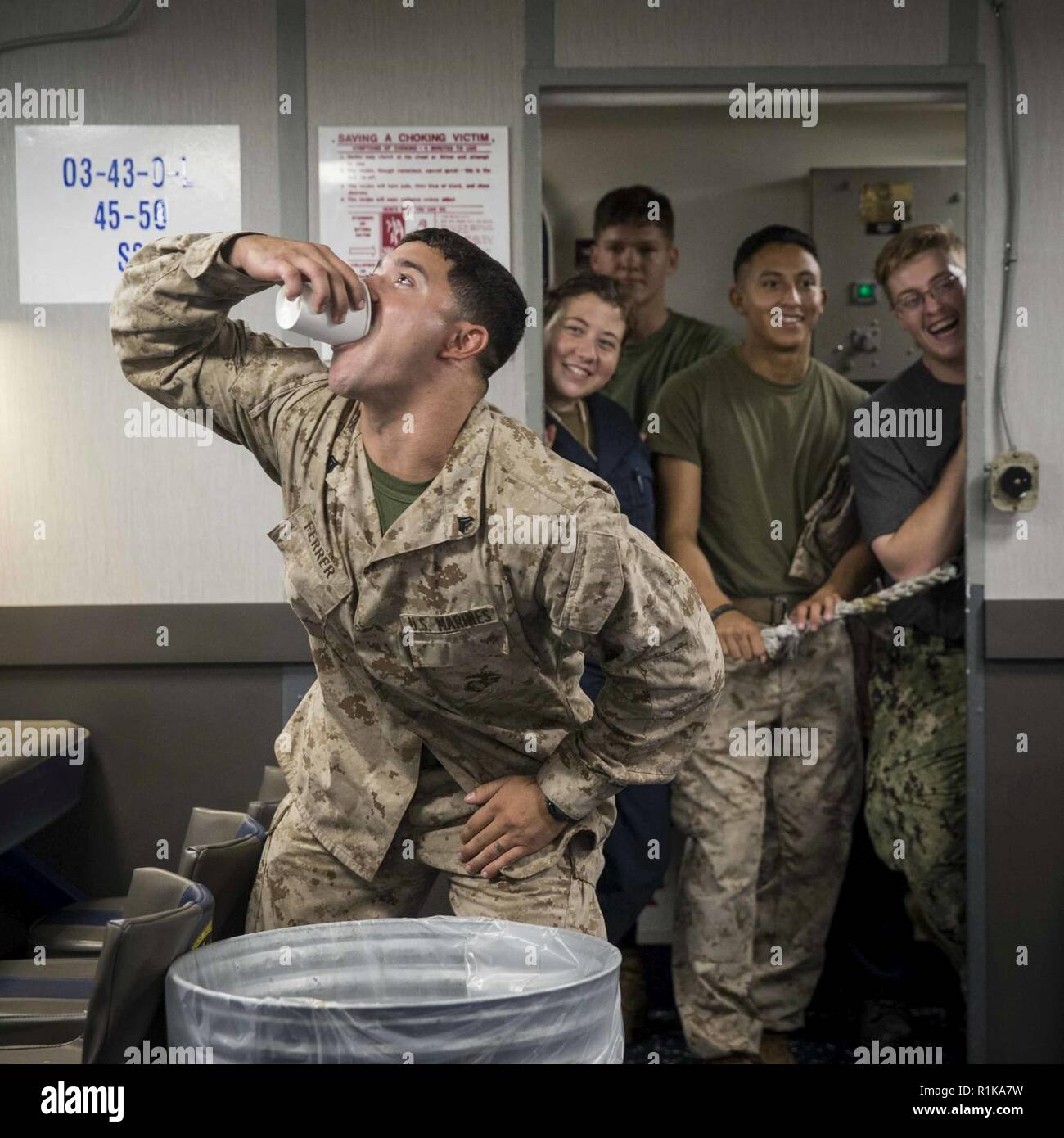 GULF OF ADEN - U.S. Marine Cpl. Amaury Ferrer, left, a wrecker operator with Combat Logistics Battalion (CLB) 13, 13th Marine Expeditionary Unit (MEU), takes a drink from the grog during a mess night for Corporal's Course aboard the Whidbey Island-class dock landing ship USS Rushmore (LSD 47), Oct. 9, 2018. The Essex Amphibious Ready Group and the 13th MEU are deployed to the U.S. 5th Fleet area of operations in support of naval operations to ensure maritime stability and security in the Central Region, connecting the Mediterranean and the Pacific through the western Indian Ocean and three str Stock Photo