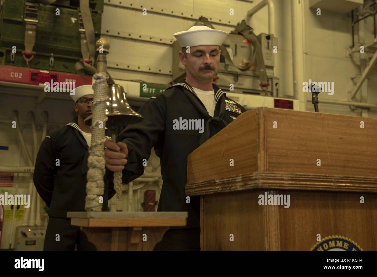 PACIFIC OCEAN (Oct. 10, 2018) Machinist’s Mate 1st Class Jared Alessi, from Buffalo, N.Y., rings the ship’s bell at the 243rd Navy birthday celebration ceremony held in the hangar bay of the amphibious assault ship USS Bonhomme Richard (LHD 6). Bonhomme Richard is operating in the U.S. 3rd Fleet area of operations. Stock Photo