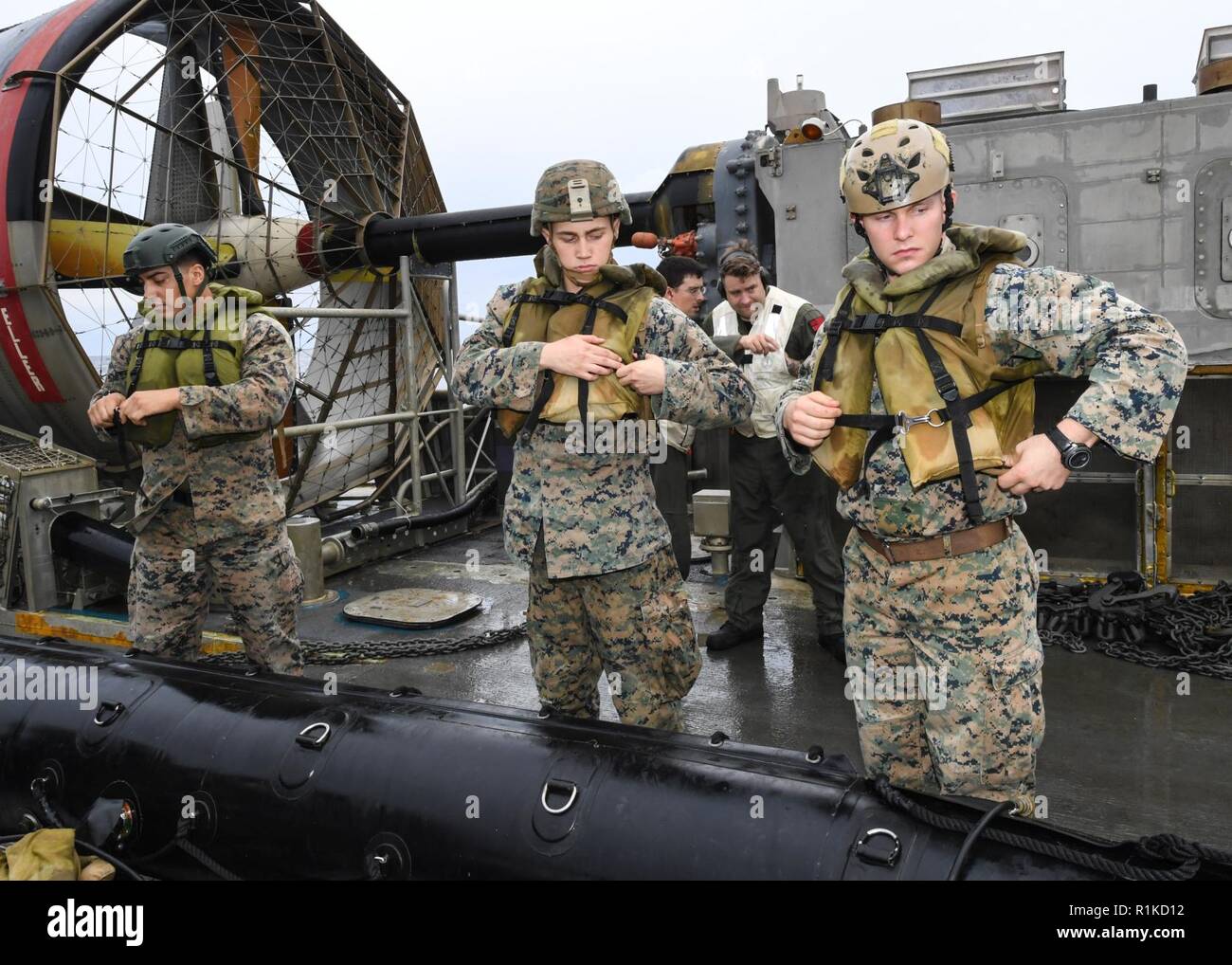 EAST CHINA SEA (Oct. 14, 2018) Sgt. Mark Weber, Lance Cpl. Jonah Massey, Luke Nierengaten, assigned to the 31st Marine Expeditionary Unit (MEU), don safety gear aboard a landing craft, air cushion, assigned to Naval Beach Unit 7, before launching a combat raiding rubber craft boat into the water during integrated unit level training. The amphibious assault ship USS Wasp (LHD 1), flagship of Wasp Amphibious Ready Group, with embarked 31st Marine Expeditionary Unit, is operating in the Indo-Pacific region to enhance interoperability with partners and serve as a ready-response force for any type  Stock Photo