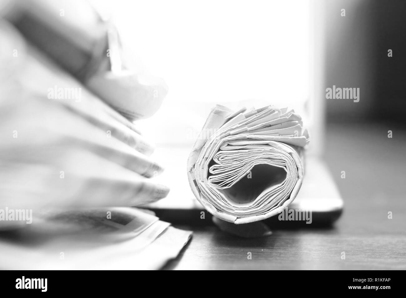 Blurred pile of newspapers with headlines, articles and rolled magazine on wooden table with light background for text (copy space), concept for news Stock Photo
