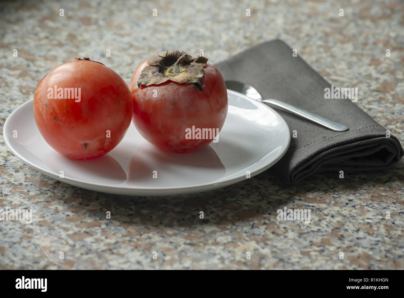 two kaki fruits in the plate with napkin and spoon Stock Photo