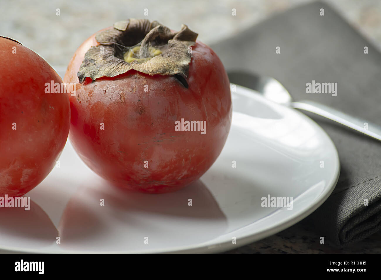 two kaki fruits in the plate with napkin and spoon close-up Stock Photo