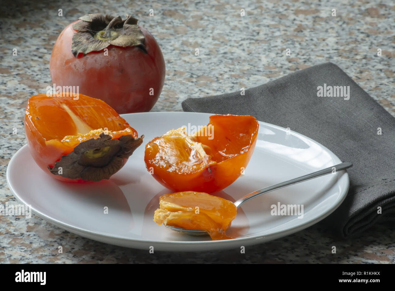 kaki fruit in the plate cut in half and full teaspoon Stock Photo